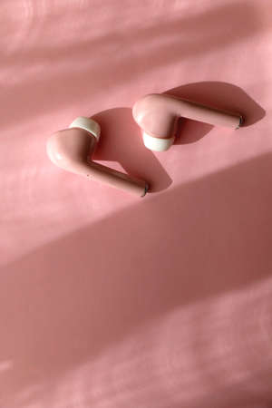 Pink wireless  earphones on pink background. Flat lay.