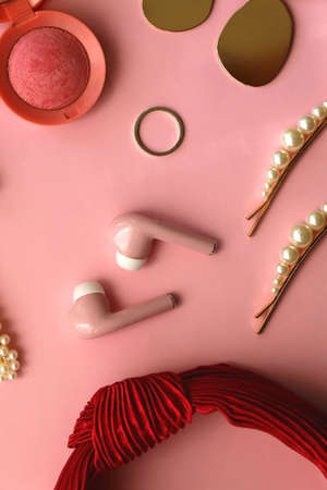 Pink  earphones, red hairband, pearl hair clips, gold earrings and ring, pink blush and lipstick on pastel pink background. Flat lay.の写真素材