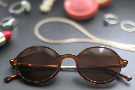 Lipstick, blush, decorative hair clips, scrunchie, sunglasses and various silver jewelry on dark gray background. Selective focus.の写真素材