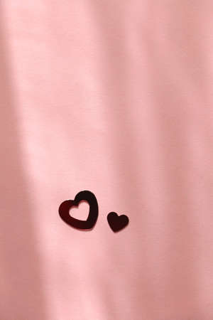 Red heart shaped confetti on pastel pink background. Flat lay.