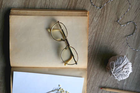 Old book, papers, various pressed flowers, eyeglasses, scissors, pencils and rope on wooden desk....