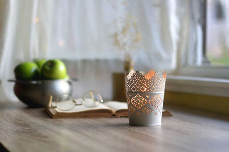 Bowl of green apples, open book, reading glasses, lit candle and flowers on the table. Selective focus.の写真素材