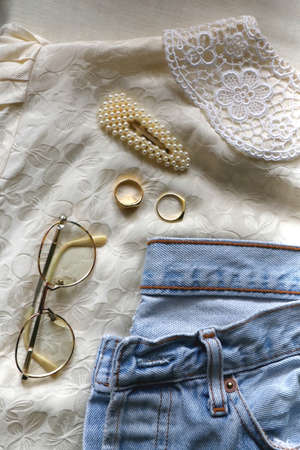 Vintage jeans, white blouse, retro eyeglasses, pearl barrette and gold rings. Fashionable outfit layout. Flat lay.の写真素材