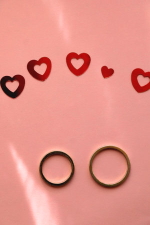 Gold wedding rings and red heart confetti on pastel pink background. Flat lay.の写真素材