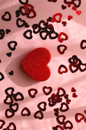 Small red heart and heart shaped confetti on pastel pink background. Flat lay.