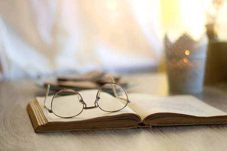 Plate of chocolate, open book, reading glasses, lit candle and flowers on the table. Selective...