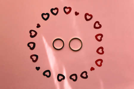 Gold wedding rings and red heart confetti on pastel pink background. Flat lay.の写真素材