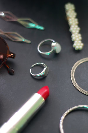 Lipstick, blush, decorative hair clips, scrunchie, sunglasses and various silver jewelry on dark...