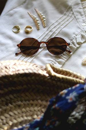 White blouse, wicker bag with tied floral scarf, tortoiseshell sunglasses, pearl hair clips and gold rings. Fashion for spring and summer. Selective focus.の写真素材
