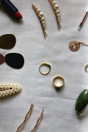Various gold jewelry, personal accessories and beauty products on neutral background. Flat lay.