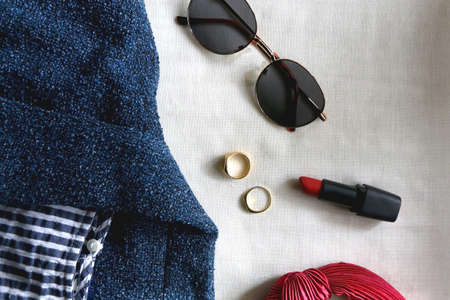 Blue jacket, striped shirt, round sunglasses, red hair band, red lipstick and gold rings. Flat lay.