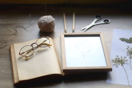 Old book, papers, various pressed flowers, eyeglasses, scissors, pencils and rope on wooden desk. Crafting and making herbarium at home. Selective focus.の写真素材