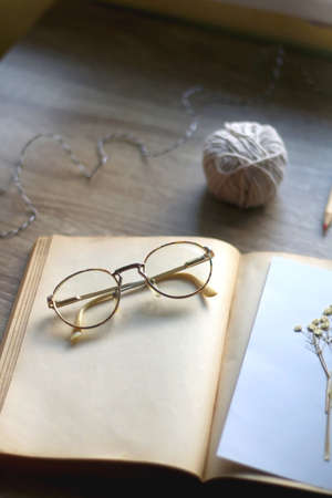 Old book, papers, various pressed flowers, eyeglasses, scissors, pencils and rope on wooden desk. Crafting and making herbarium at home. Selective focus.の写真素材