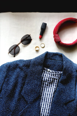 Blue jacket, striped shirt, round sunglasses, red hair band, red lipstick and gold rings. Flat lay.