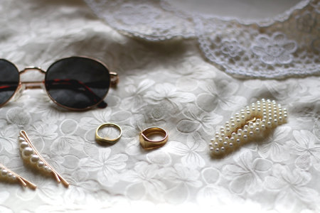 Vintage white floral blouse, round sunglasses, gold rings and pearl hair barrettes. Selective focus.