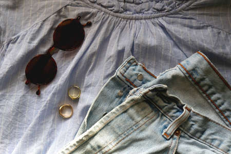 Blue striped blouse, light wash jeans, round sunglasses and gold rings. Flat lay.の写真素材
