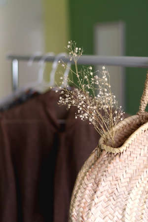 Straw bag, gypsophila flowers and neutral clothes on a clothing rack. Selective focus.の写真素材
