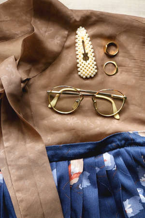 Brown blouse, blue skirt, vintage eyeglasses, gold rings and pearl barrette. Outfit details, flat lay.の写真素材