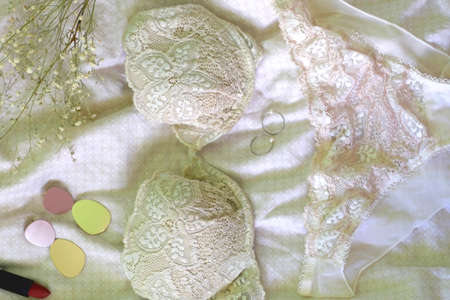 Beige lace lingerie set, gold accessories, lipstick and gypsophila flowers on the bed. Flat lay.の写真素材