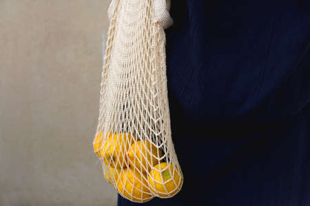 Unrecognizable person wearing crochet bag with fresh lemons. Selective focus.