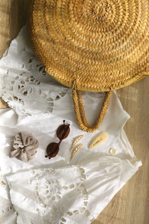 White linen lace shirt, round straw bag, sunglasses and cute hair accessories on wooden background. Flat lay.の写真素材