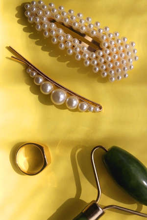 Round sunglasses, lipstick, jade roller, ring and hair accessories on bright yellow background. Flat lay.の写真素材