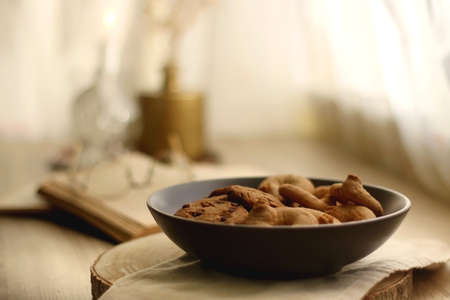 Plate of chocolate chip cookies and sugar cookies, vintage books and reading glasses, candle and flower on the table. Hygge at home. Selective focus.の写真素材
