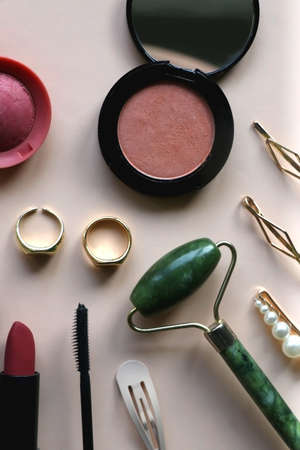 Gingham scrunchie, blush and highlighter, gold rings, various hair clips, jade roller, lipstick and mascara on beige background. Flat lay.の写真素材