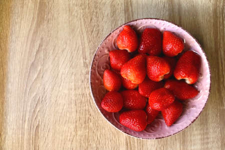 Pink bowl full of fresh strawberries on wooden table. Flat lay.の写真素材