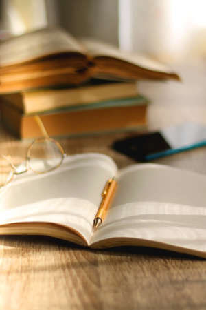 Open book, mechanical pencil, reading glasses, mobile phone and strack of books on the desk....
