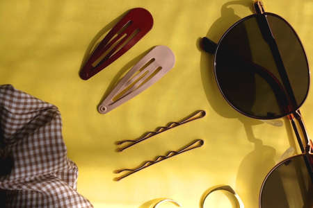 Retro sunglasses, gold rings, various hair accessories and make up products on vibrant yellow background. Flat lay.の写真素材