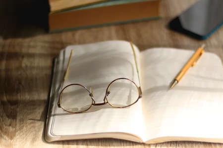Open book, mechanical pencil, reading glasses, mobile phone and strack of books on the desk....