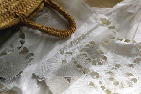 White linen lace blouse and round straw bag on wooden background. Selective focus.の写真素材