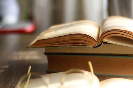 Open book and reading glasses on the table, illuminated by sunlight. Stack of vintage books in the background. Selective focus.の写真素材