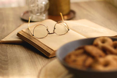 Plate of chocolate chip cookies and sugar cookies, vintage books and reading glasses, candle and flower on the table. Hygge at home. Selective focus.の写真素材