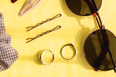 Retro sunglasses, gold rings, various hair accessories and make up products on vibrant yellow...
