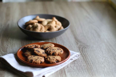 Plate of chocolate chip cookies and bowl of sugar cookies on wooden table. Selective focus.の写真素材