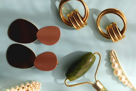 Coral blush, jade roller, pearl barrettes and gold earrings on bright blue background. Flat lay.の写真素材