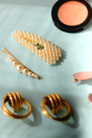 Coral blush, jade roller, pearl barrettes and gold earrings on bright blue background. Selective focus.の写真素材