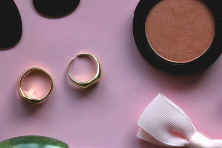 Pink scrunchie, gold earrings and rings, blush, various hair barrettes, lipstick and jade roller on bright pink background. Flat lay.の写真素材