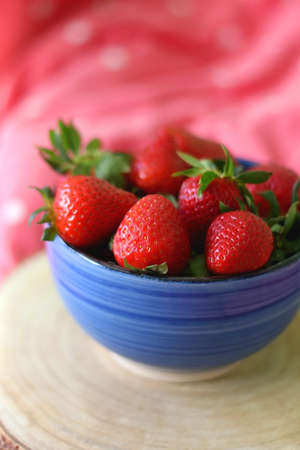 Bowl of fresh strawberries on a bed with colorful bedding. Selective focus.の写真素材