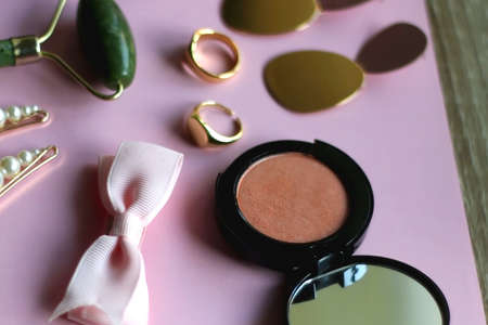 Pink scrunchie, gold earrings and rings, blush, various hair barrettes, lipstick and jade roller on bright pink background. Selective focus.の写真素材