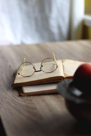 Silver bowl filled with red apples, open book and reading glasses on the table. Selective focus.の写真素材