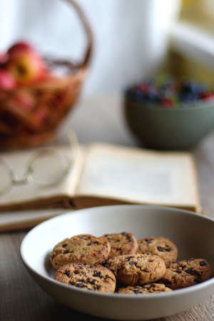 Bowl of strawberries and blueberries, open books with reading glasses, plate of chocolate chip...