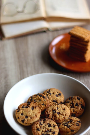 Bowl of chocolate chip cookies, plate of biscuits, open books and reading glasses on the table....