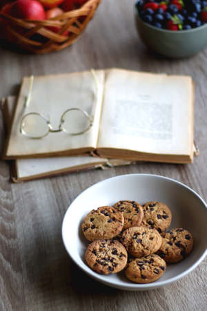Bowl of strawberries and blueberries, open books with reading glasses, plate of chocolate chip...