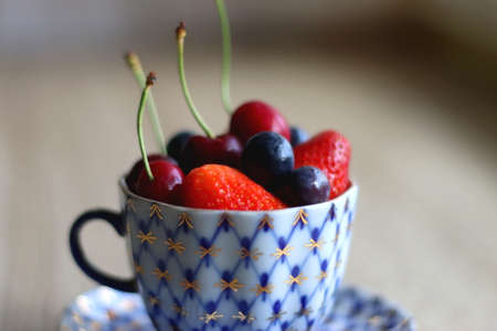 Vintage porcelain cup filled with strawberries, blueberries and cherries. Selective focus.の写真素材