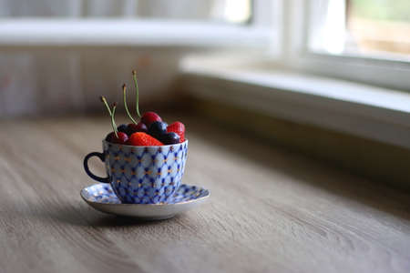 Vintage porcelain cup filled with strawberries, blueberries and cherries. Selective focus.の写真素材