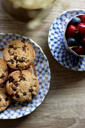 Plate of chocolate chip cookies, cup filled with strawberries, blueberries and cherries, open book...
