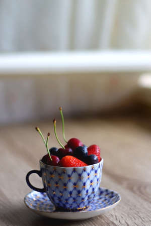 Vintage porcelain cup filled with strawberries, blueberries and cherries. Selective focus.の写真素材